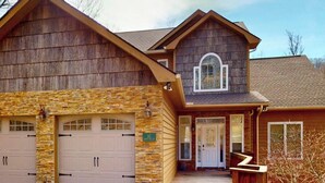 A two-story house with a stone facade, a garage with two doors, and a front door with a small porch. - Breeze on Inn • Deck, Firepit, & Game Room (Sugar Mountain)