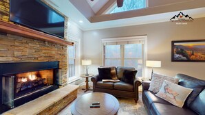 A living room with a stone fireplace, leather sofas, a coffee table, and a painting on the wall. - Breeze on Inn • Deck, Firepit, & Game Room (Sugar Mountain)