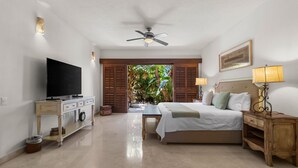 A bedroom with a bed, bedside lamps, a TV, a ceiling fan, and a view of greenery outside. - Pelicano. Beachfront 2 floor condo in Bucerias (Bucerías)