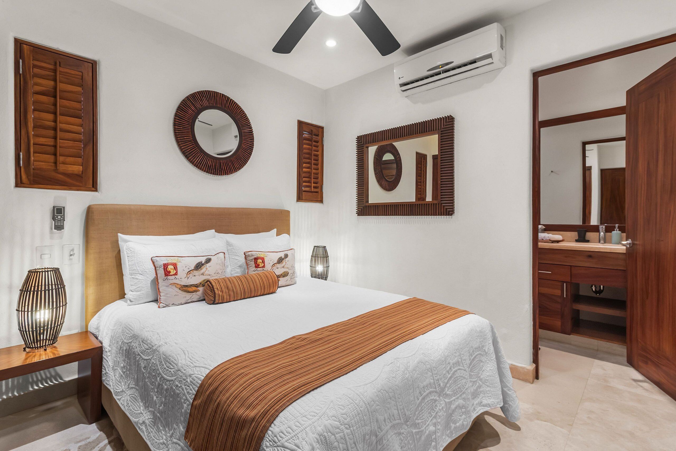 A hotel room with a large bed, a wooden headboard, a round mirror, and a built-in vanity with a mirror.