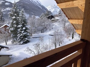 A wooden cabin with a view of a snowy landscape, including trees and mountains.