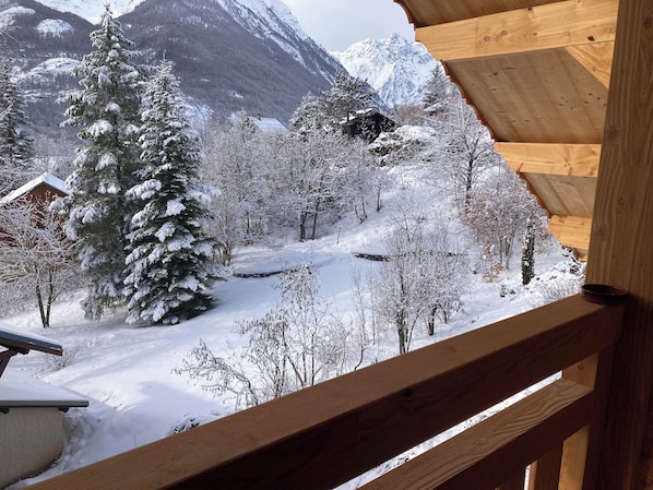 A wooden cabin with a view of a snowy landscape, including trees and mountains.
