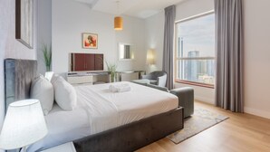 A modern hotel room with a large bed, a desk, a chair, and a view of the city.