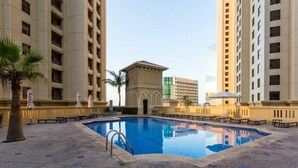 A swimming pool surrounded by high-rise buildings, with palm trees and lounge chairs.
