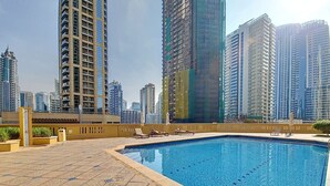Una piscina en la azotea con solárium de baldosas, rodeada de edificios altos.
