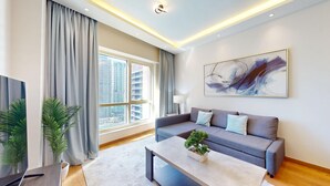 A modern living room with a grey sofa, a coffee table with a plant, and a large window with curtains.