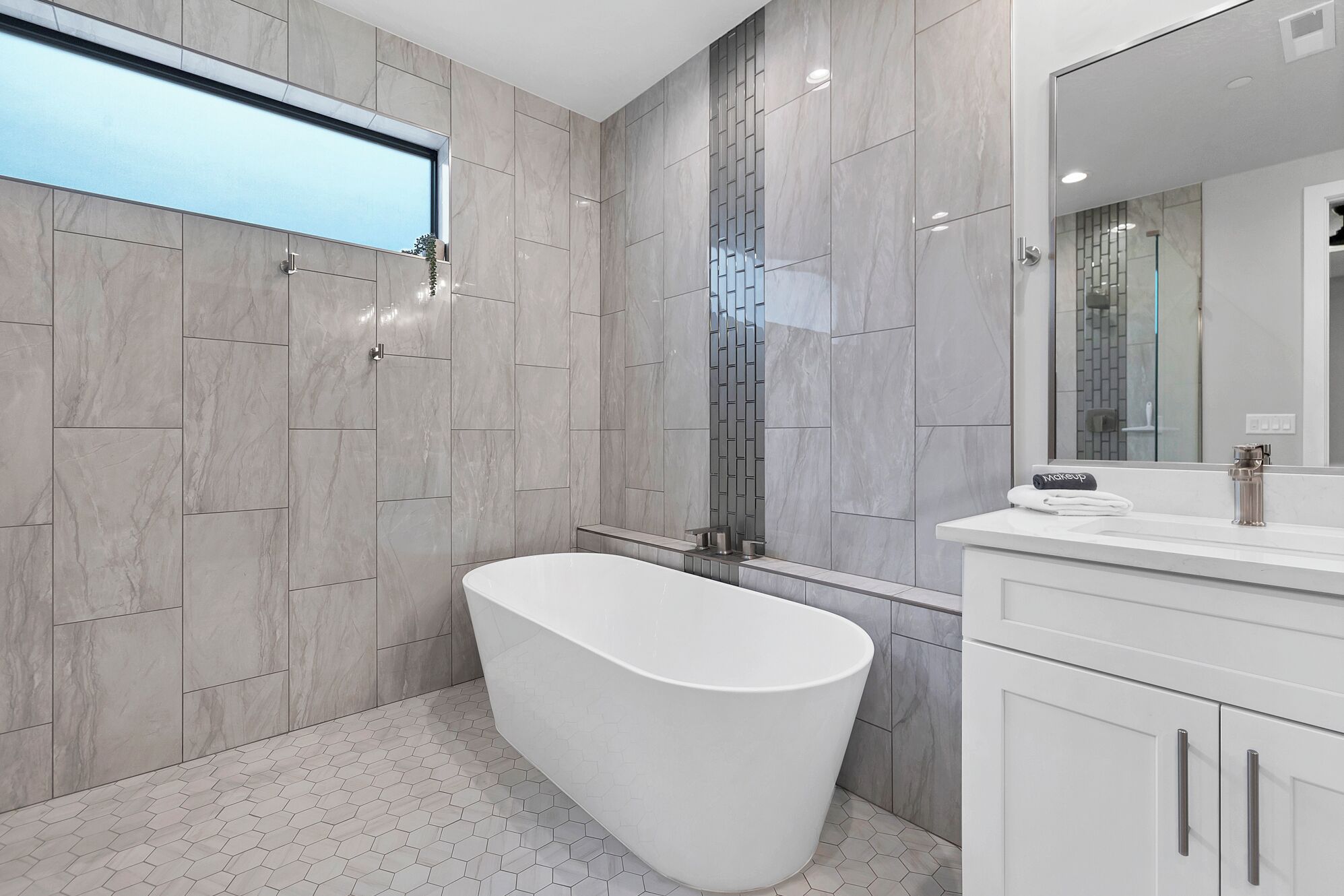 Un baño moderno con una bañera independiente, un espejo grande y un tocador con espacio para maquillaje.
