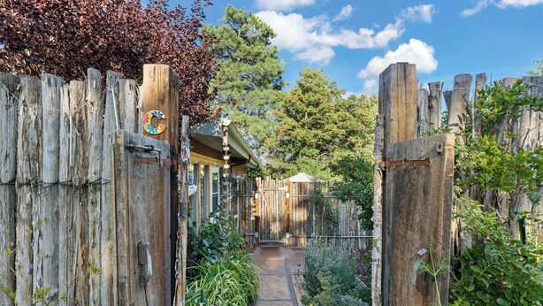 A rustic wooden gate leading to a covered outdoor area with a wooden structure and a pathway.