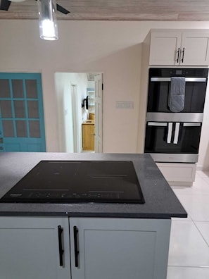 A kitchen with a black induction cooktop, white cabinets, a blue door, and a stainless steel oven. - Four bed / 3 bath villa in Holetown, Sleeps 8 adults +babies - 30ft private pool (Sunset Crest, Holetown)