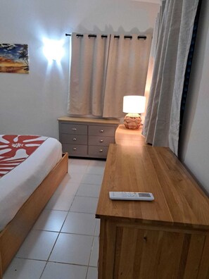 Une chambre d’hôtel avec un lit, une table de chevet en bois, une télécommande, une lampe et une fenêtre avec des rideaux.