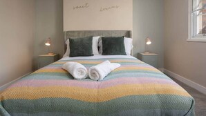 Een net opgemaakt bed met een gestreept laken, twee kussens en twee opgerolde handdoeken. Aan weerszijden van het bed staan twee nachtlampen.