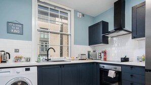 Een moderne keuken met donkere kastjes, een ingebouwde wasmachine, een raam en een roestvrijstalen afzuigkap.