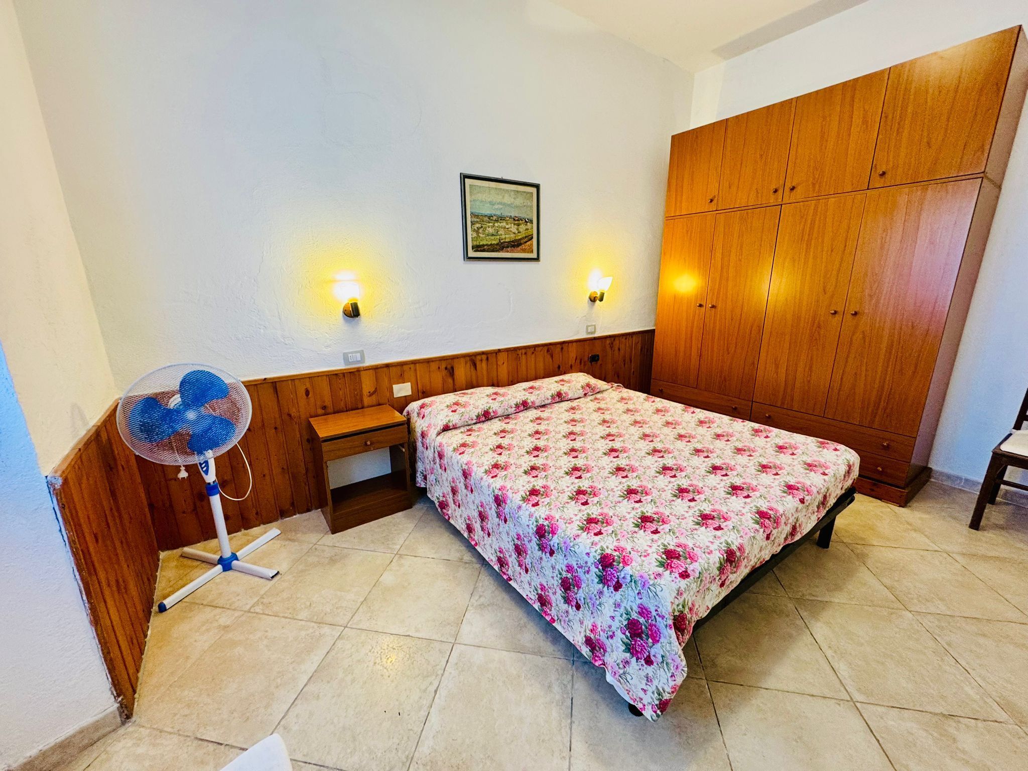 Quarto com cama, guarda-roupa de madeira, abajures e um quadro na parede.