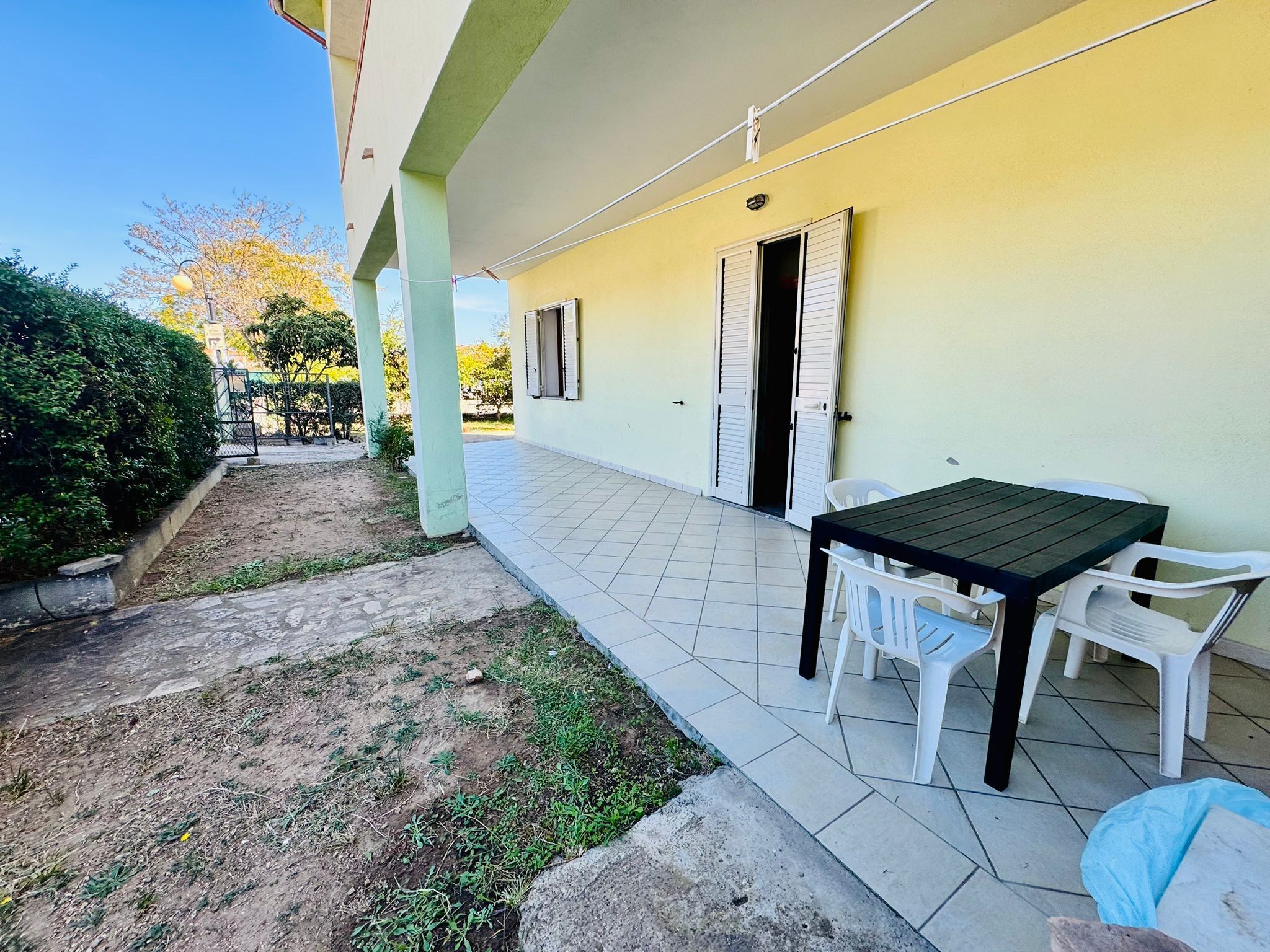 An outdoor patio area with a table and chairs, a covered seating area, and a building with a yellow wall and white shutters.