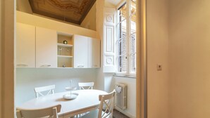 Ein Essbereich mit weißem Tisch und Stühlen, einem Heizkörper und einem Fenster mit Rollläden.