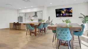 A modern kitchen with white cabinets, a stainless steel refrigerator, and a built-in oven. There is a dining area with a wooden table and teal chairs. - Charming LOFT - Downtown CL - Rooftop - BBQ - Playhouse Sq - Pets OK - Parking (Cleveland)