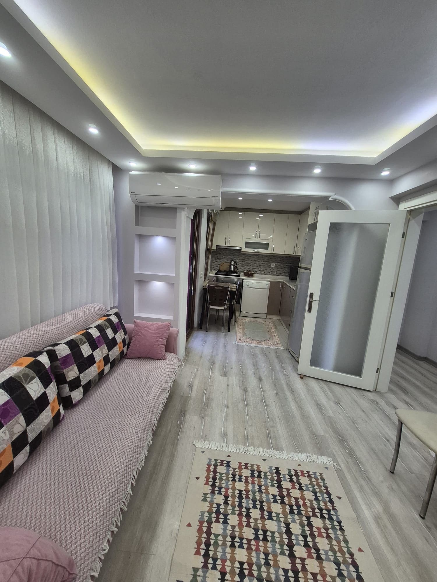 Una sala moderna con un sofá, un tapete estampado y una zona de cocina con armarios y un microondas.