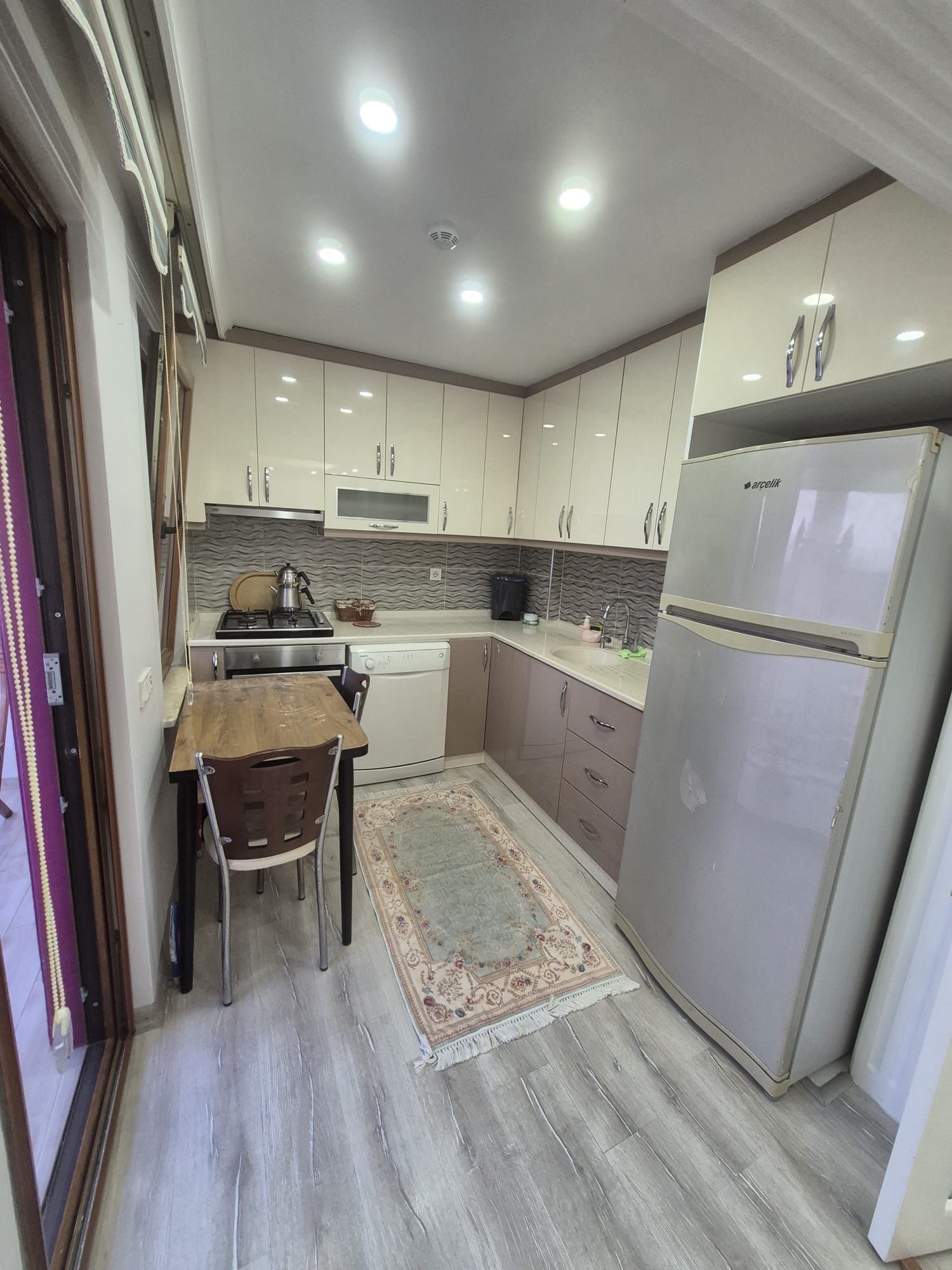 A compact kitchen with a refrigerator, stove, sink, and a small dining area with a rug.