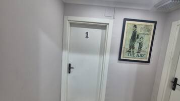 A hallway with a white door marked with the number 1, a framed poster of 'The Kid' on the wall, and a ceiling with recessed lighting.