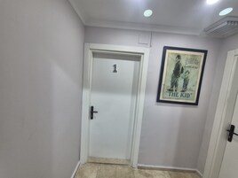 Un pasillo con una puerta blanca marcada con el número 1, un cartel enmarcado de 'The Kid' en la pared, e iluminación empotrada en el techo.