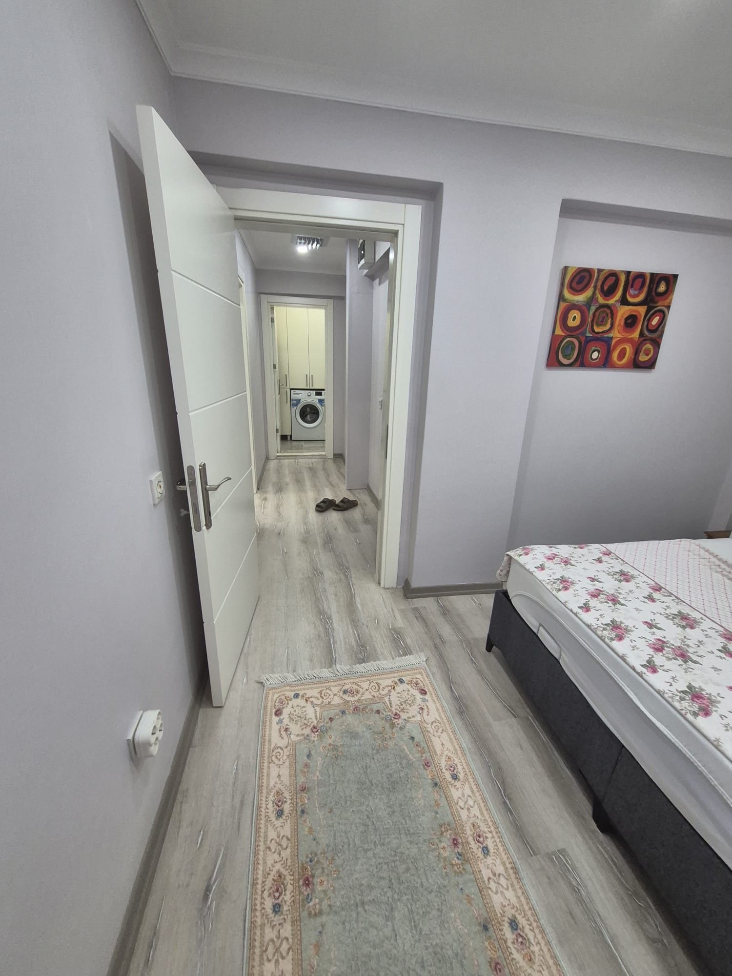 A bedroom with a bed, a rug, and a wall with a colorful painting.