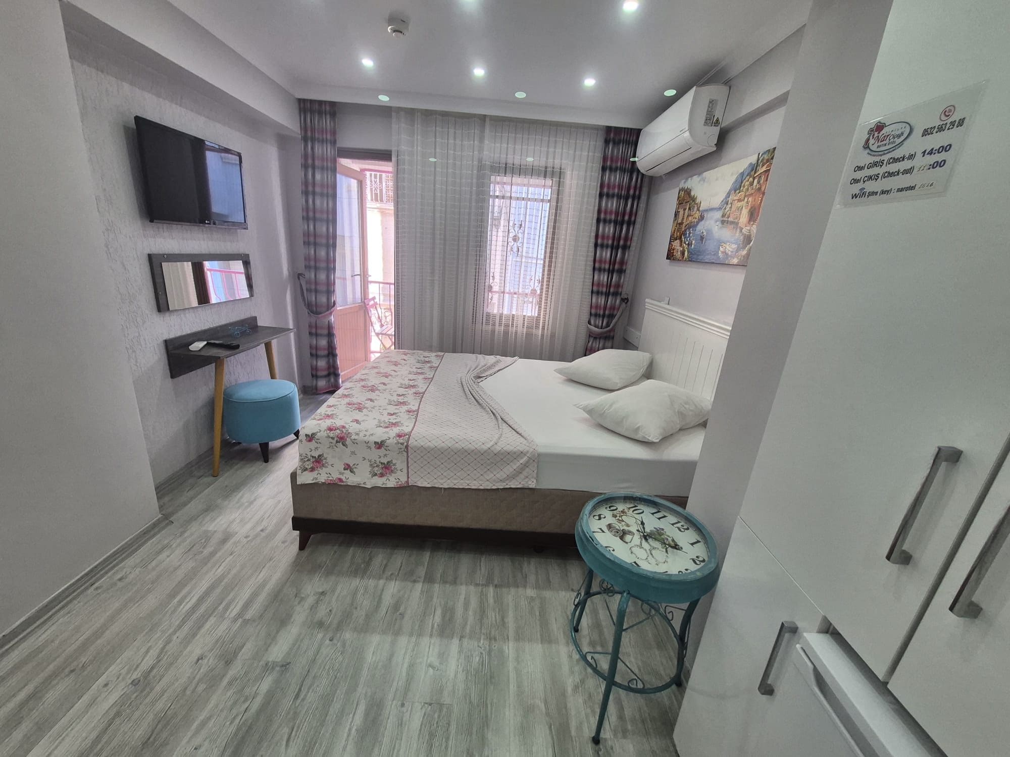 Habitación de hotel con cama, escritorio, silla, televisor y ventana con cortinas.