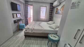 Habitación de hotel con cama, escritorio, silla, televisor y ventana con cortinas.
