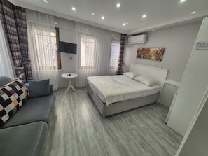Habitación de hotel con cama, sofá, mesita, televisor y aire acondicionado.