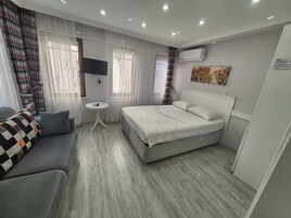 Habitación de hotel con cama, sofá, mesita, televisor y aire acondicionado.