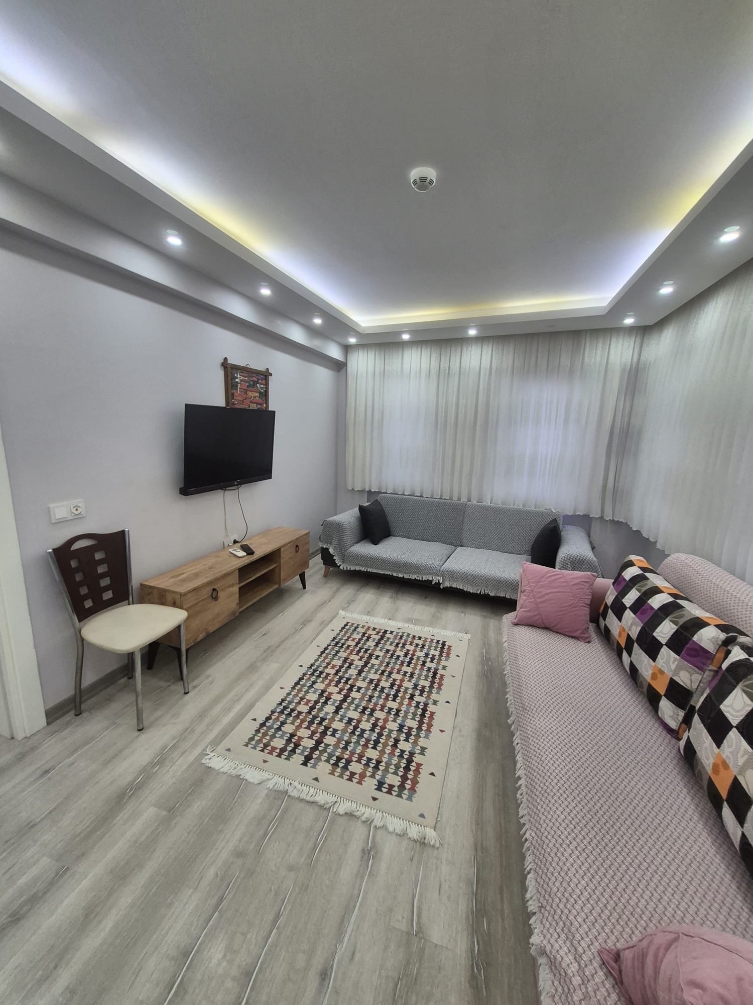 Una sala moderna con un televisor de pantalla plana, un sofá, un tapete estampado y una mesita de madera.