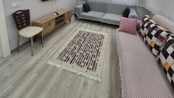 Una sala moderna con un televisor de pantalla plana, un sofá, un tapete estampado y una mesita de madera.
