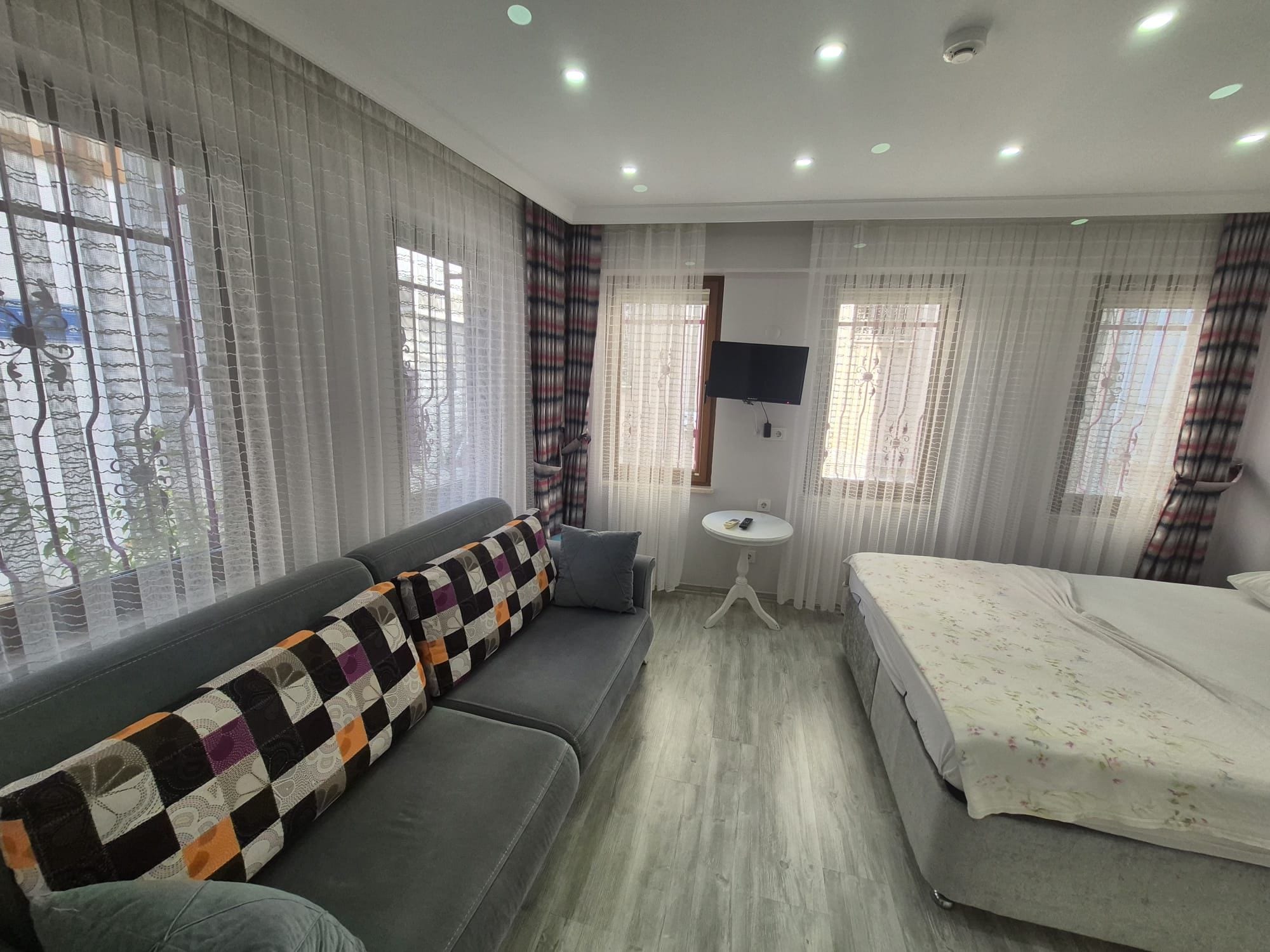 Quarto de hotel com sofá, cama, mesa redonda pequena e TV fixada na parede.
