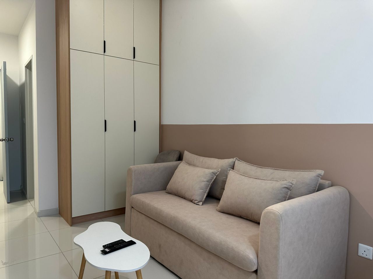 Un salon moderne avec un canapé beige, une petite table d’appoint blanche et une armoire aux portes coulissantes.