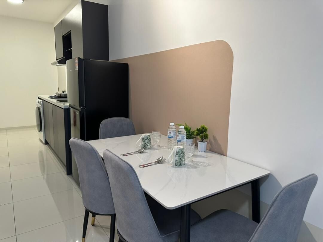 A modern kitchen with a black refrigerator, a washing machine, and a dining area with a white table and grey chairs.