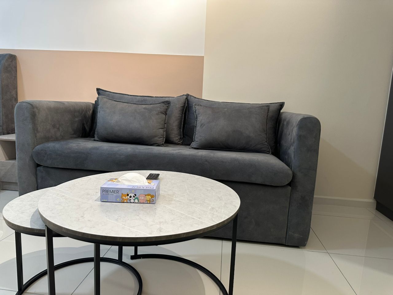 Ein graues Sofa mit zwei Kissen und einem kleinen runden Tisch, auf dem eine Fernbedienung und eine Schachtel liegen.