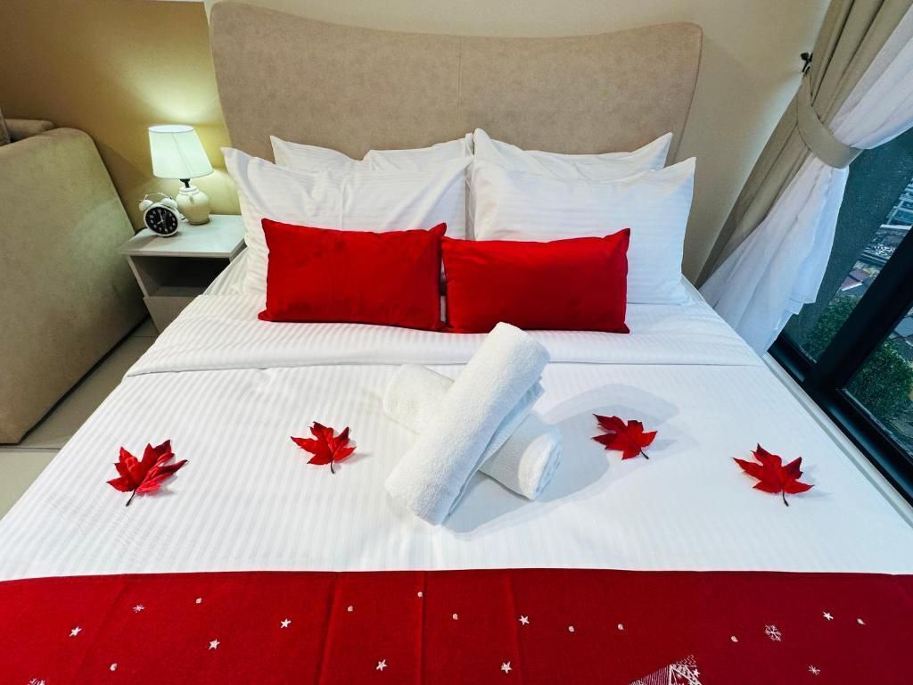 Una cama bien hecha con sábanas blancas, almohadas rojas y una manta roja con estrellas blancas.