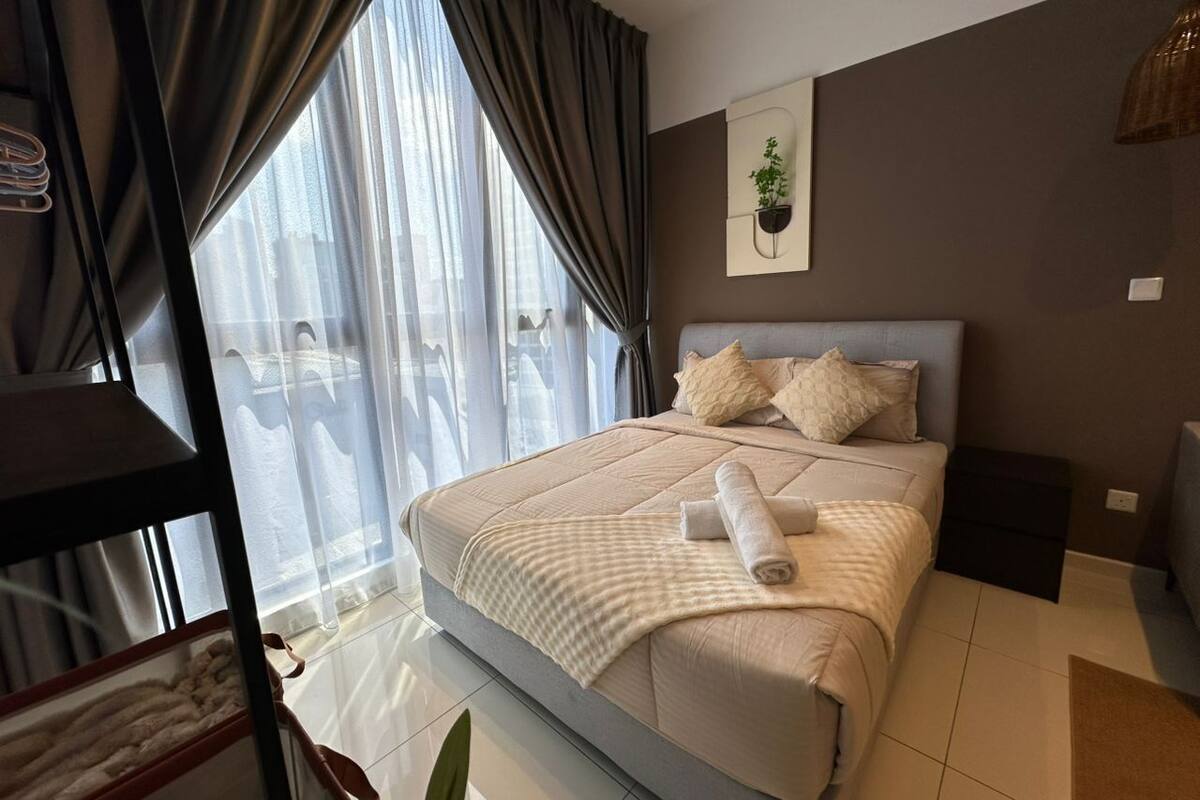 Ein modernes Schlafzimmer mit einem großen Bett, einem Nachttisch, einer kleinen Pflanze und Blick ins Freie durch transparente Vorhänge.
