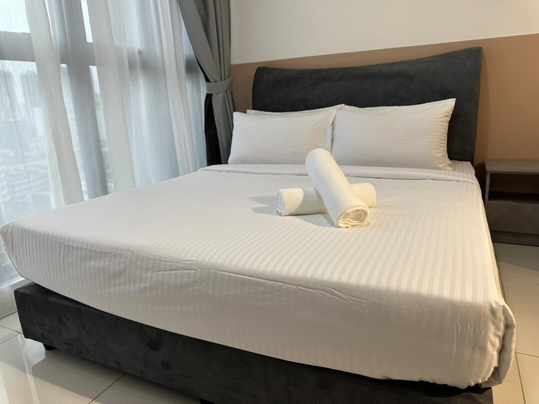 A neatly made bed with white linens and a rolled towel, a dark headboard, and a small bedside table.
