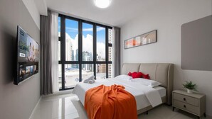 Una habitación de hotel moderna con una cama grande, una mesita de noche, un televisor y un ventanal con vistas a la ciudad.