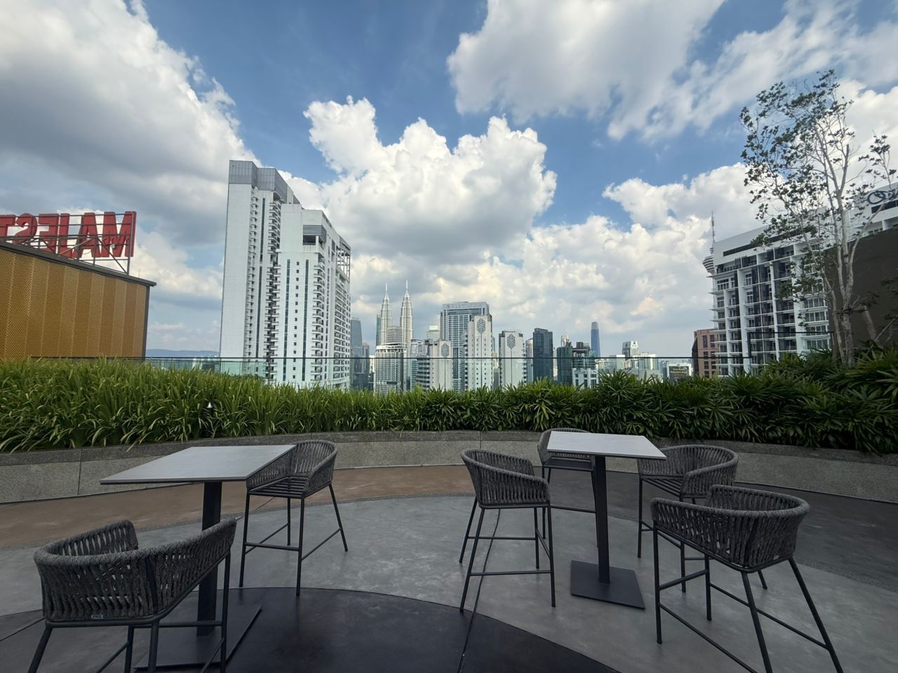 An outdoor seating area with tables and chairs, overlooking a city skyline with high-rise buildings.