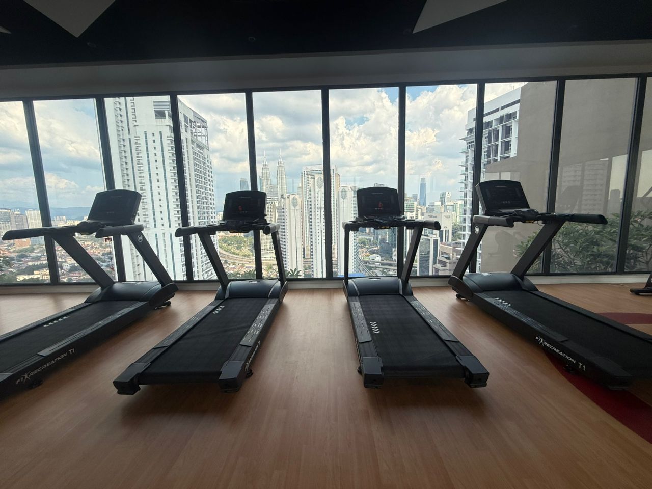 A gym with four treadmills aligned in a row, large windows offering a city view.