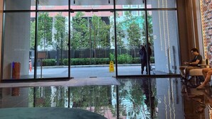 Un moderno vestíbulo de hotel con piso reflectante, techo de listones de madera y una amplia entrada de vidrio.