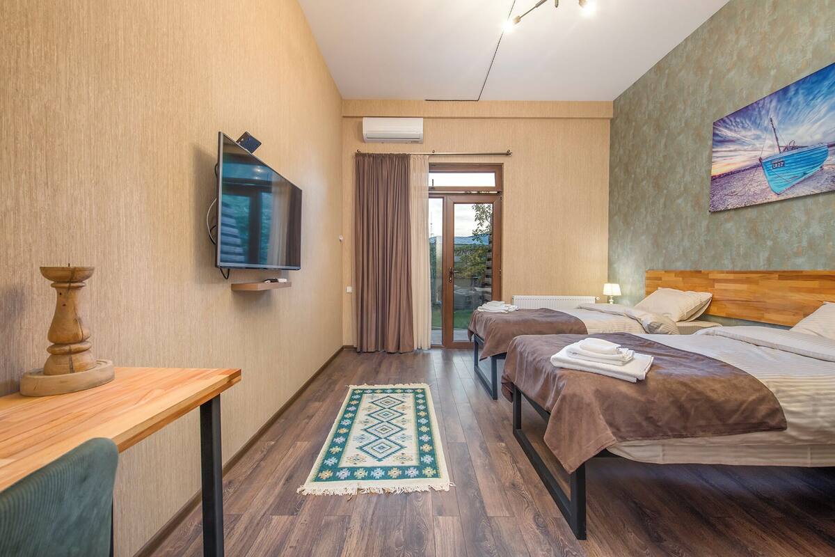 Een hotelkamer met twee bedden, een televisie, een houten nachtkastje, een kamerkleed met patroon en een schilderij aan de muur.