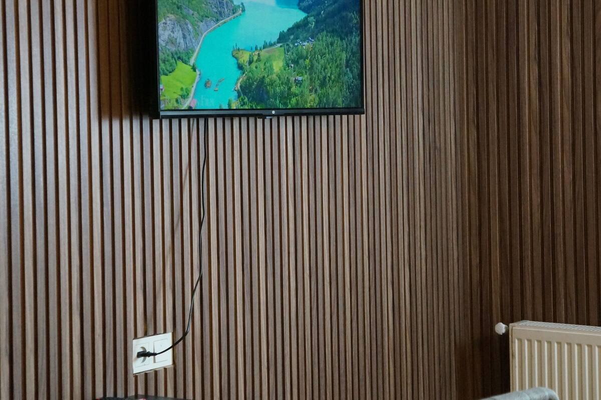 Een kamer met een televisie aan een houten lambrisering, een tafel en een stoel.