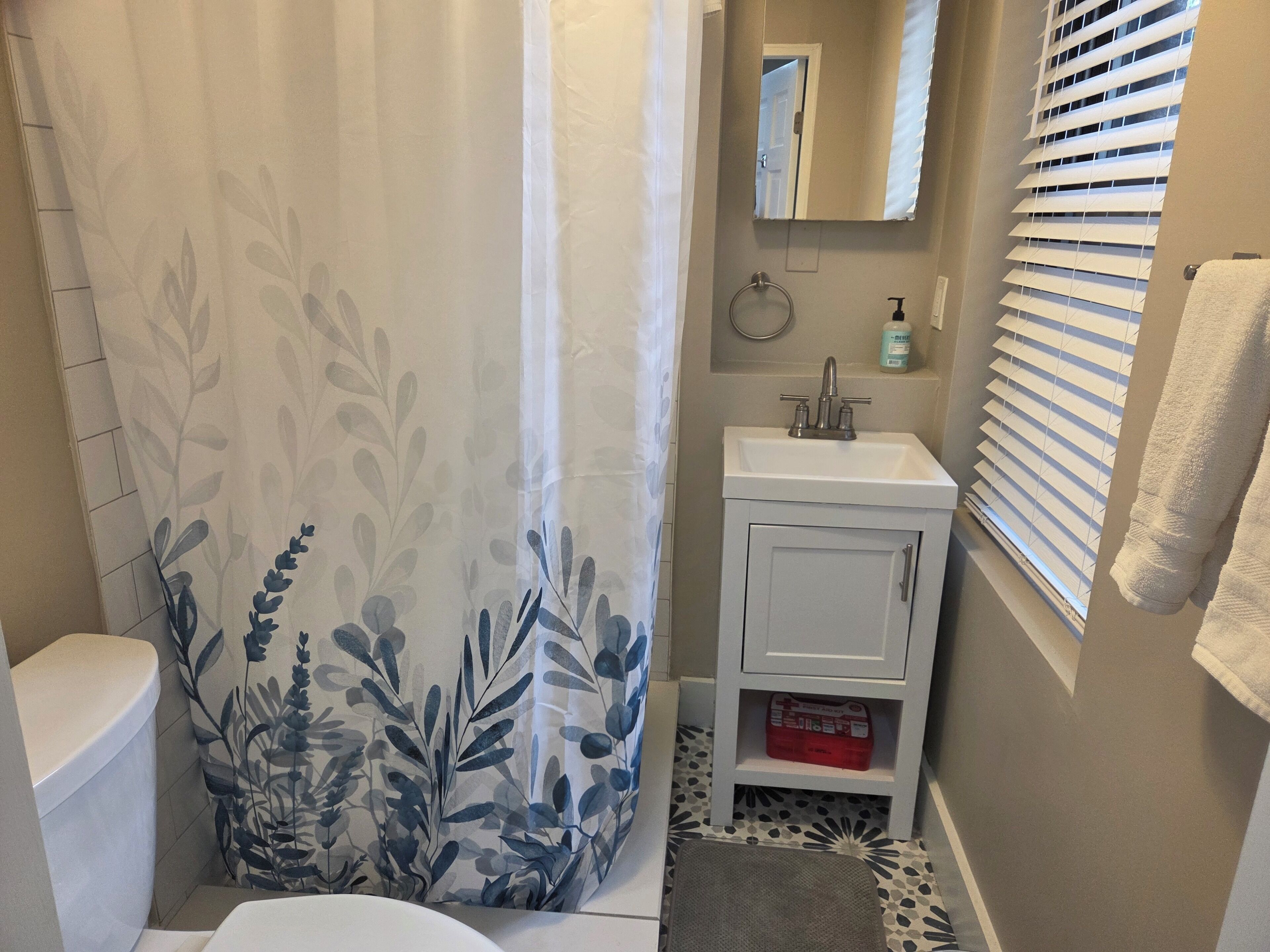 Un baño con inodoro, lavabo, espejo y cortina de ducha con estampado de hojas.