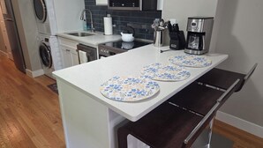 Una cocina con una isla central, lavadora, cafetera y un reloj en la pared.