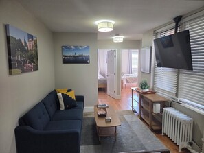 A living room with a dark blue sofa, a coffee table, a TV mounted on the wall, and a radiator. - Beacon Hill 2brm/1.5bath (Boston)