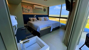 A bedroom with a bed, a desk, and a window with a view of the beach. - Setai Aquamaris Vista Mar - By Almare (João Pessoa)