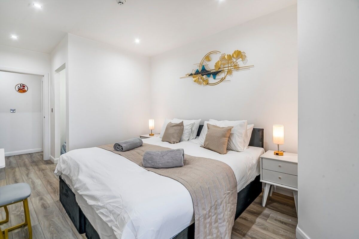 Une chambre moderne avec un grand lit, deux tables de chevet, un élément décoratif fixé au mur et une porte ornée d’un logo circulaire.