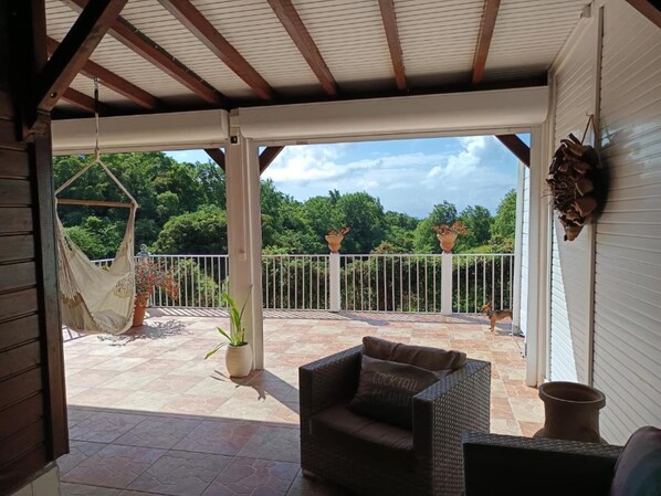 A covered patio with a wicker sofa, a hammock, and potted plants.